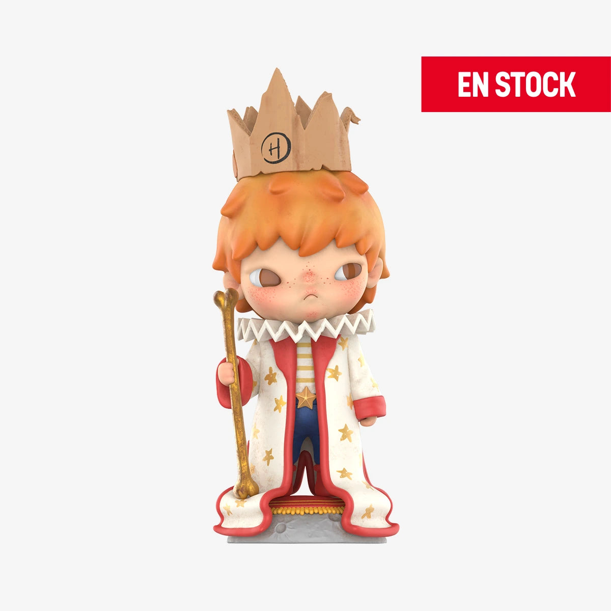Figura coleccionable de Hirono con temática de principito, vestido con una capa blanca decorada con estrellas doradas, una corona de cartón con la letra "H" y un cetro dorado. El personaje tiene cabello naranja, pecas y una expresión seria. En la esquina superior derecha aparece una etiqueta roja con el texto "EN STOCK"