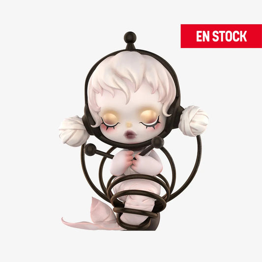 Figura coleccionable de SKULLPANDA de la serie "Image of Reality", representando a un personaje con ojos cerrados y expresión serena, envuelto en una estructura de aros negros con extremos esféricos. Su cuerpo es blanco con detalles rosados y una flor al nivel de las piernas. En la esquina superior derecha aparece una etiqueta roja con el texto "EN STOCK"