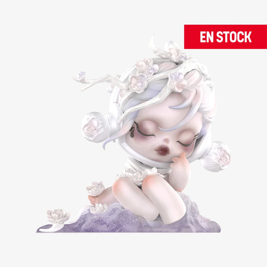 Figura coleccionable de SKULLPANDA de la serie "Ink Plum Blossom", mostrando a un personaje etéreo de piel perlada, sentado sobre una base lila decorada con flores blancas. Tiene los ojos cerrados, expresión tranquila y detalles florales en el cabello y alrededor del cuerpo. En la esquina superior derecha aparece una etiqueta roja con el texto "EN STOCK"